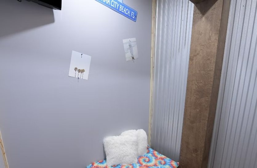 The Florida Luxury Suite — private beach-themed room with a tie-dye bed, fluffy pillows, and a Panama City Beach sign